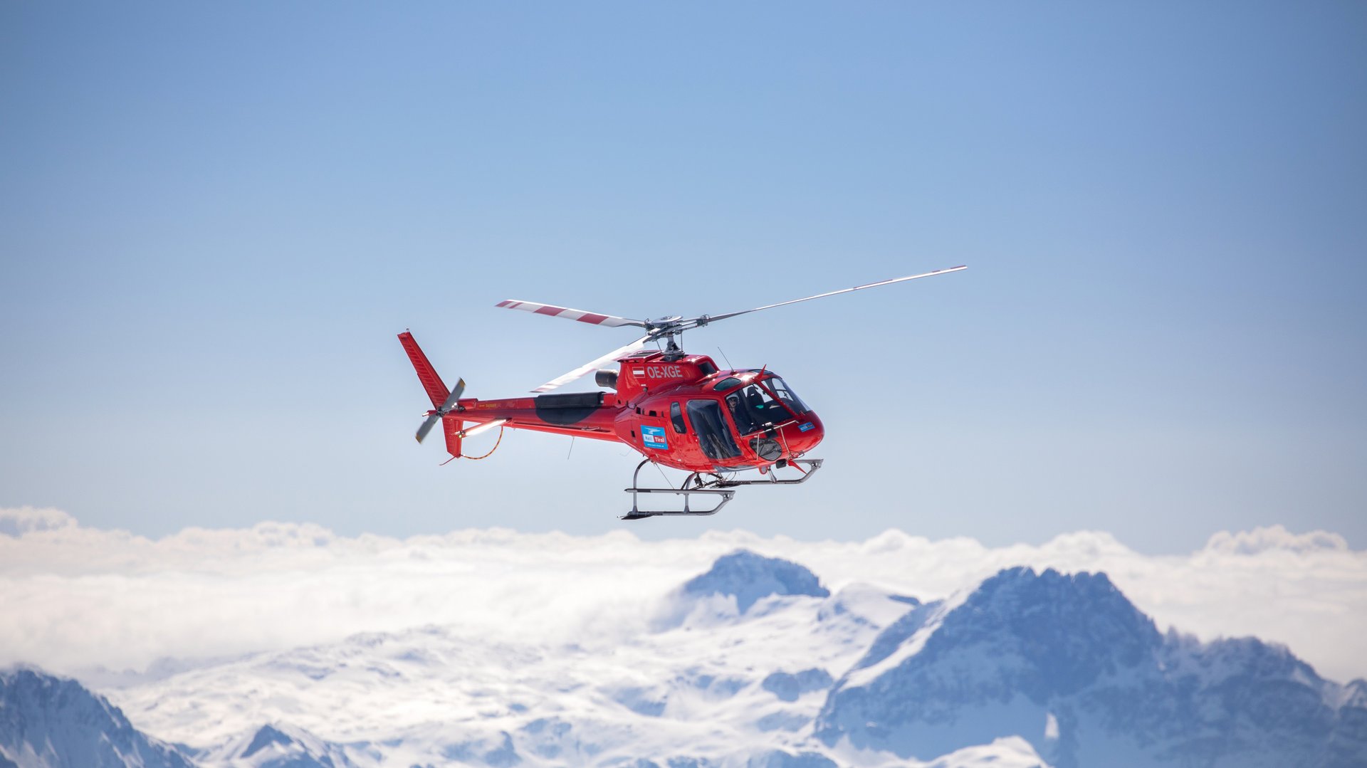 Helikopter über schneebedeckten Bergen Ein roter Helikopter fliegt über schneebedeckte Berge unter klarem Himmel. Der Blick ist aus der Luft.