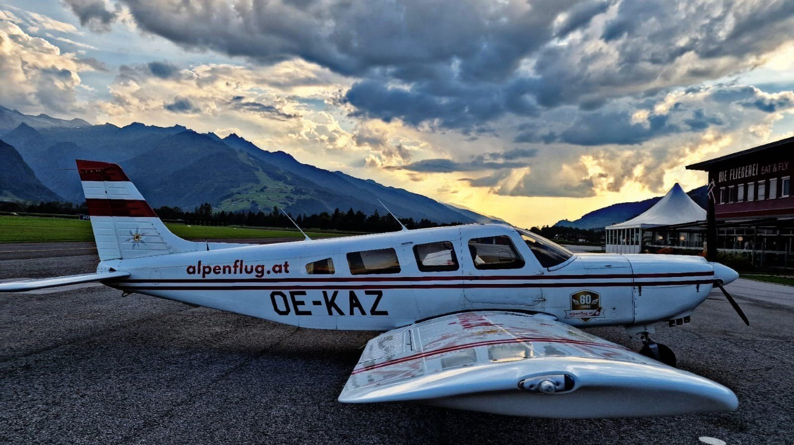 Piper Flugzeug am Flugfeld Parkendes Piper Flugzeug auf einem Flugfeld mit Bergen im Hintergrund und bewölktem Himmel