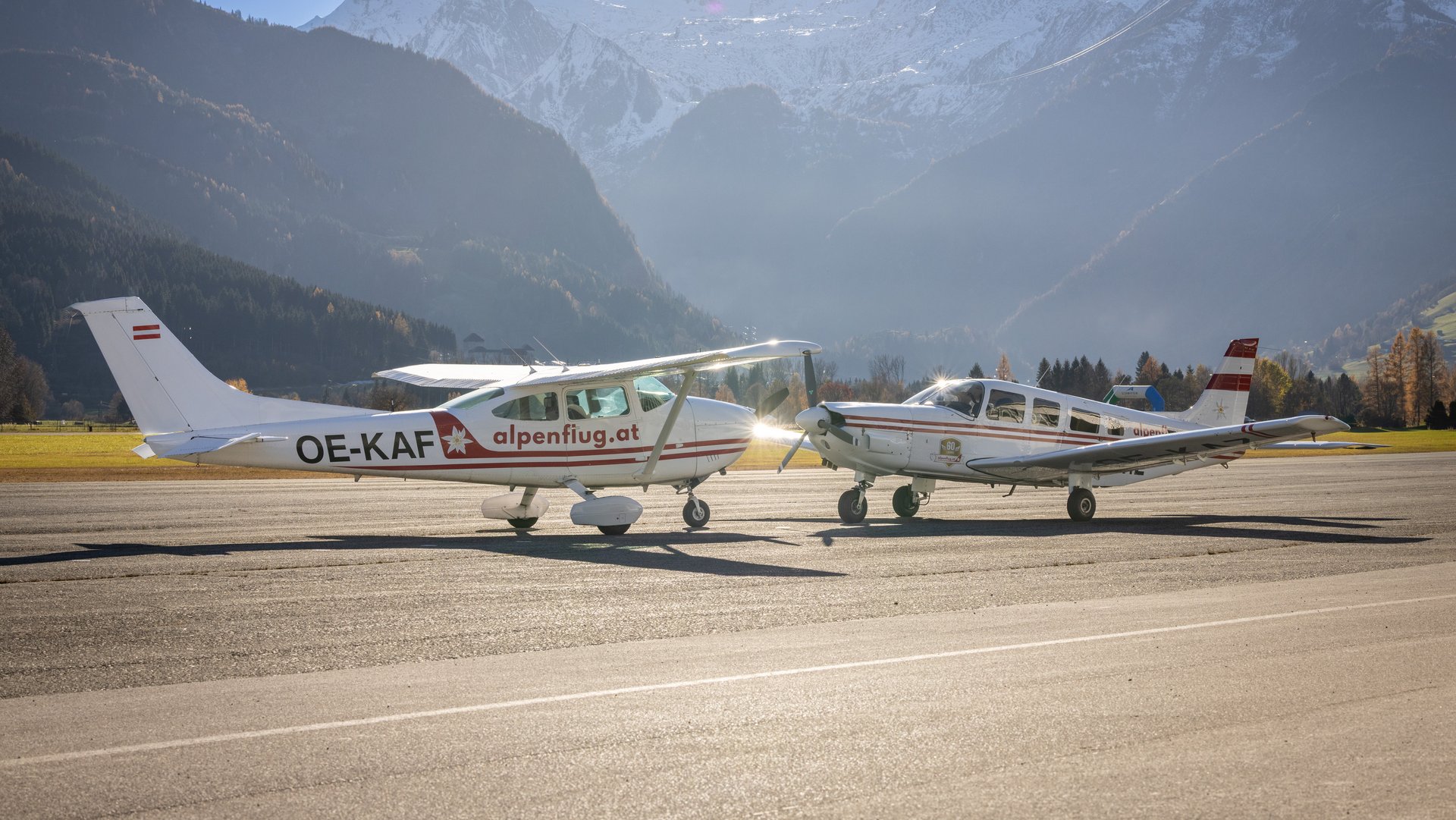 Flugzeuge vor Bergkulisse Zwei kleine Flugzeuge auf einer Landebahn mit Bergen im Hintergrund und blauem Himmel